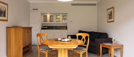 A dining area with a round wooden table, two chairs, and a small side table with a glass of white wine.