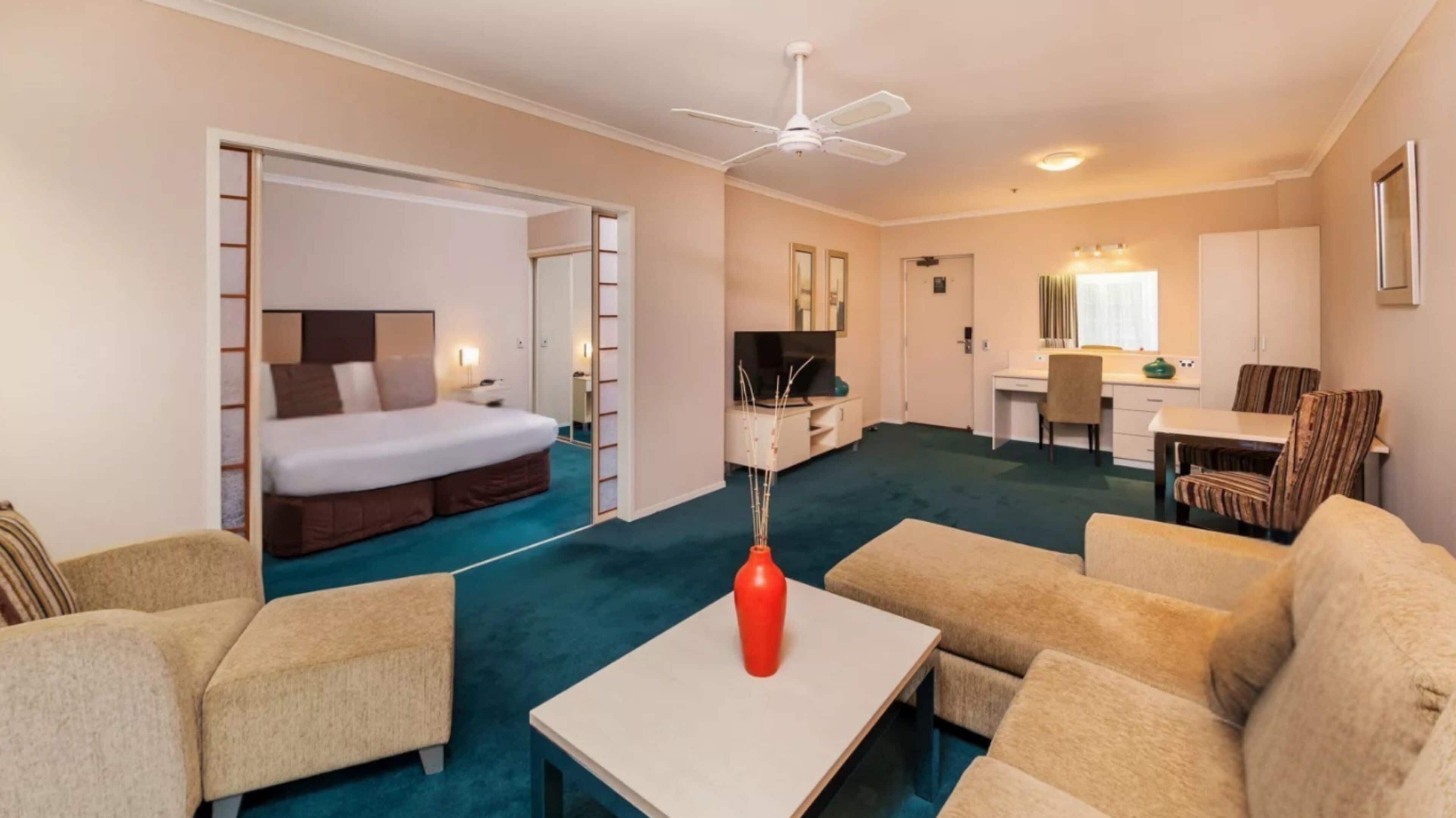 A hotel room with a bed, a desk, a chair, a TV, and a dining table.