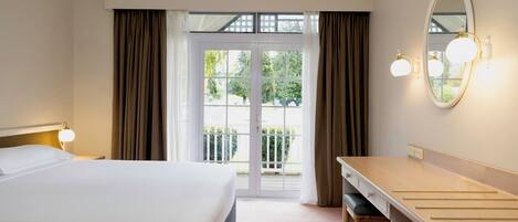 A hotel room with a bed, a desk, a mirror, and a view of the outdoors through a glass door.