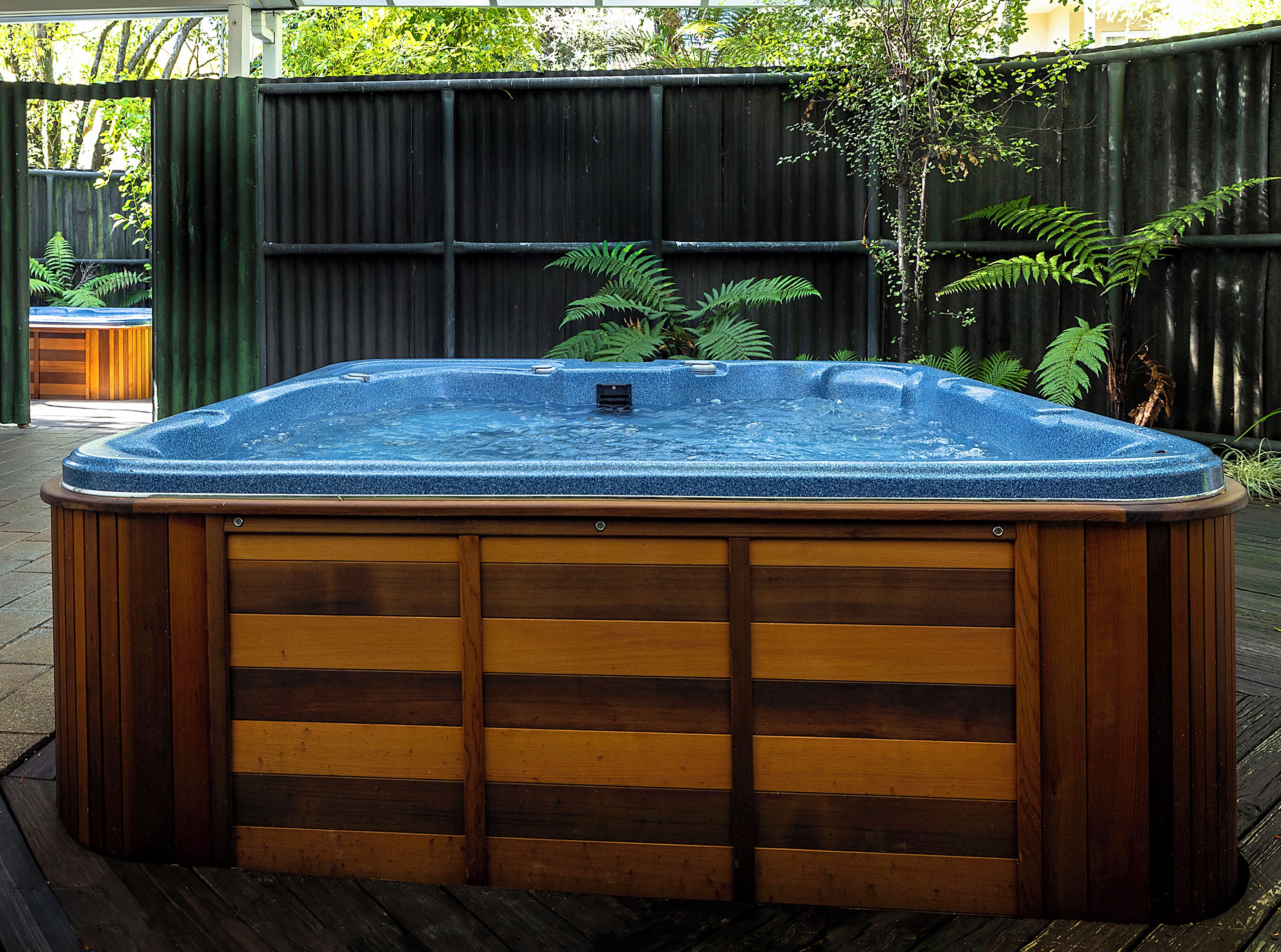 A hot tub with a wooden exterior and a metal top, surrounded by a wooden deck and a metal fence.