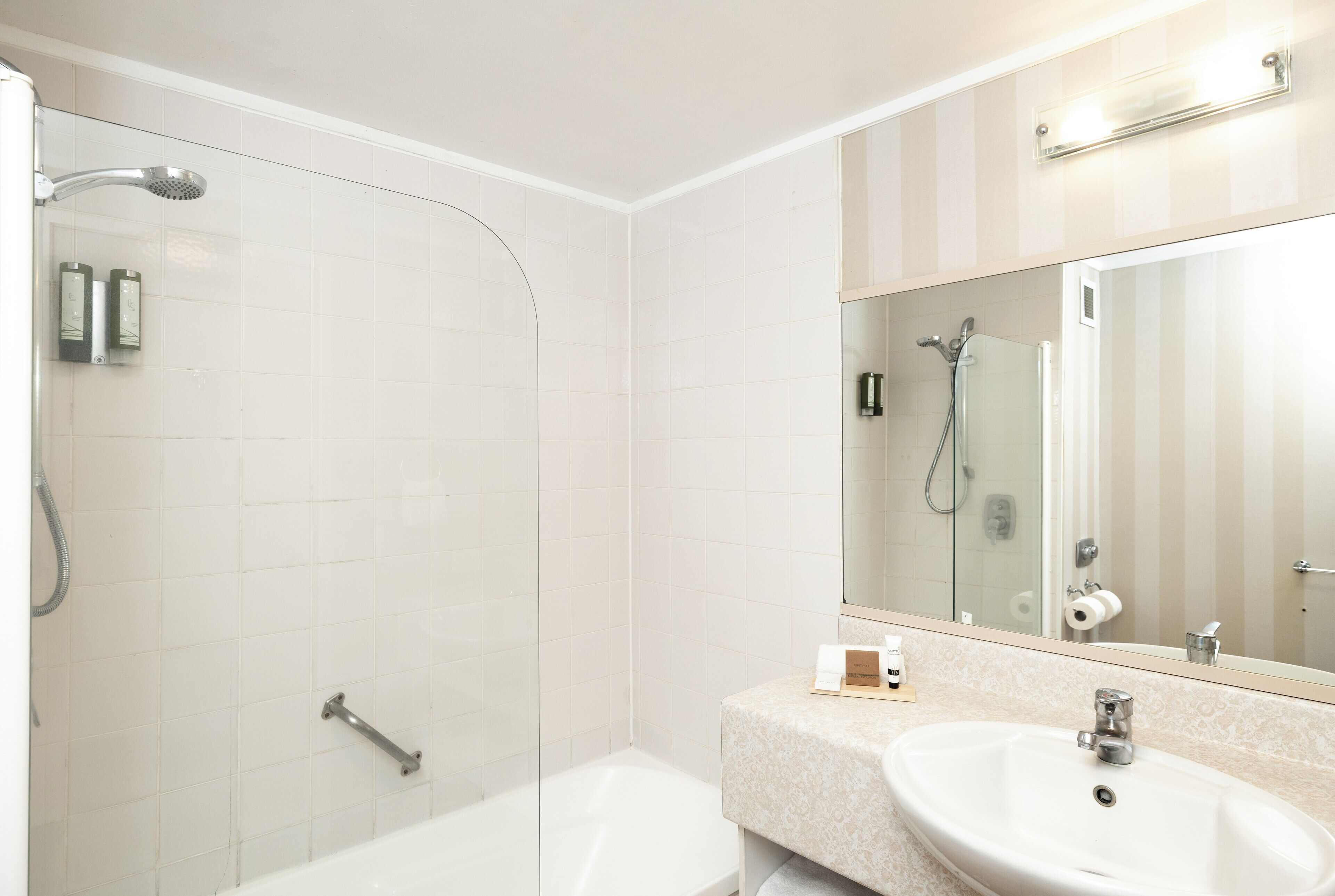 Un baño moderno con ducha de vidrio, bañera independiente y tocador con lavamanos y espejo.
