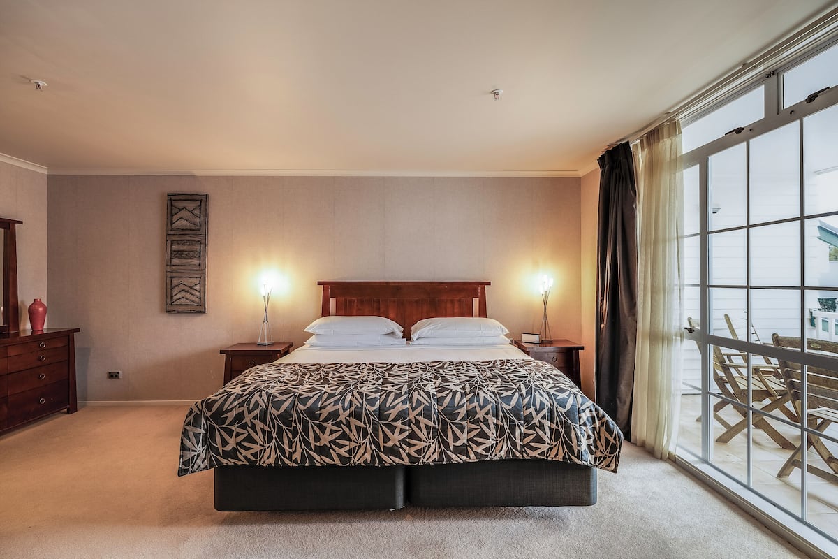 Een slaapkamer met een groot bed, twee nachtkastjes, een dressoir en uitzicht buiten door een groot raam.