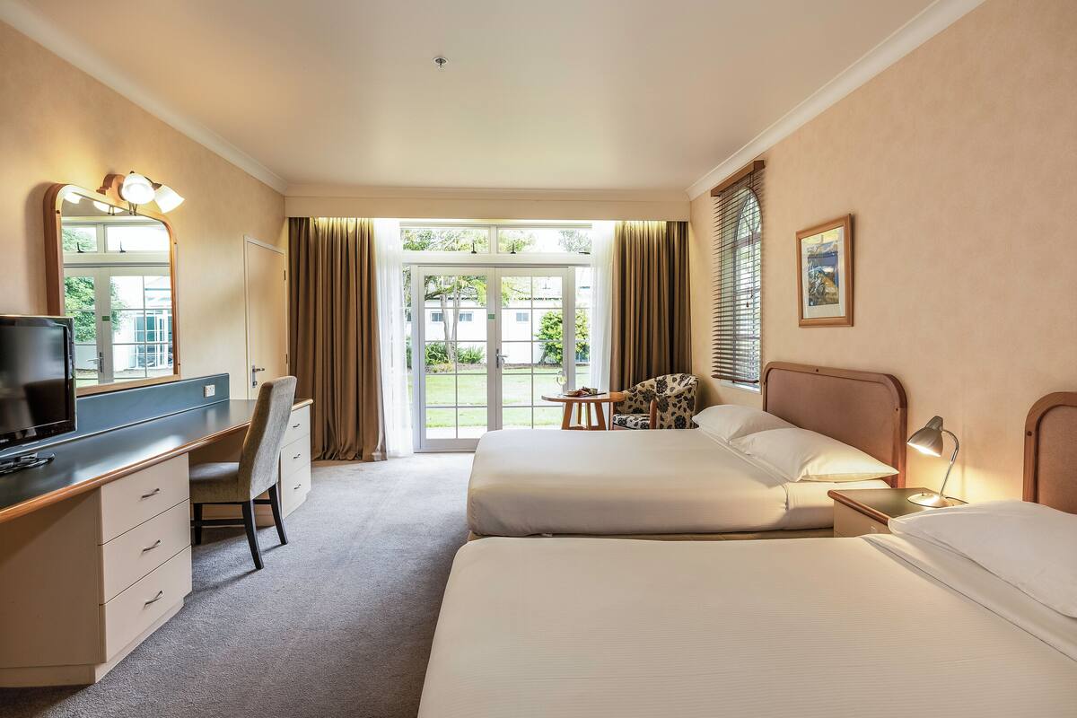 Een hotelkamer met twee bedden, een bureau met stoel, een televisietoestel en een raam met gordijnen.