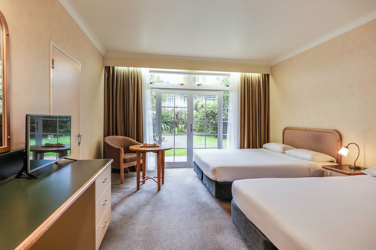 Een hotelkamer met twee bedden, een bureau, een stoel, een televisie en uitzicht op de omgeving.
