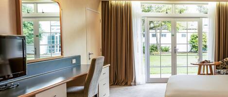 A hotel room with a bed, a desk with a chair, a television, a large mirror, and a view of the outdoors through a glass door.
