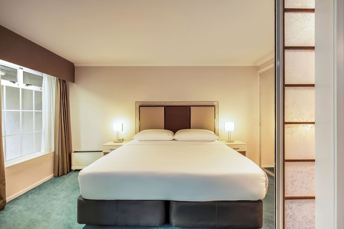 Een hotelkamer met een groot bed, twee nachtkastjes, een raam met gordijnen en uitzicht op het omliggende landschap.
