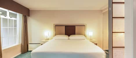 Ein Hotelzimmer mit einem großen Bett, zwei Nachttischen, einem Fenster mit Vorhängen und Blick nach draußen.