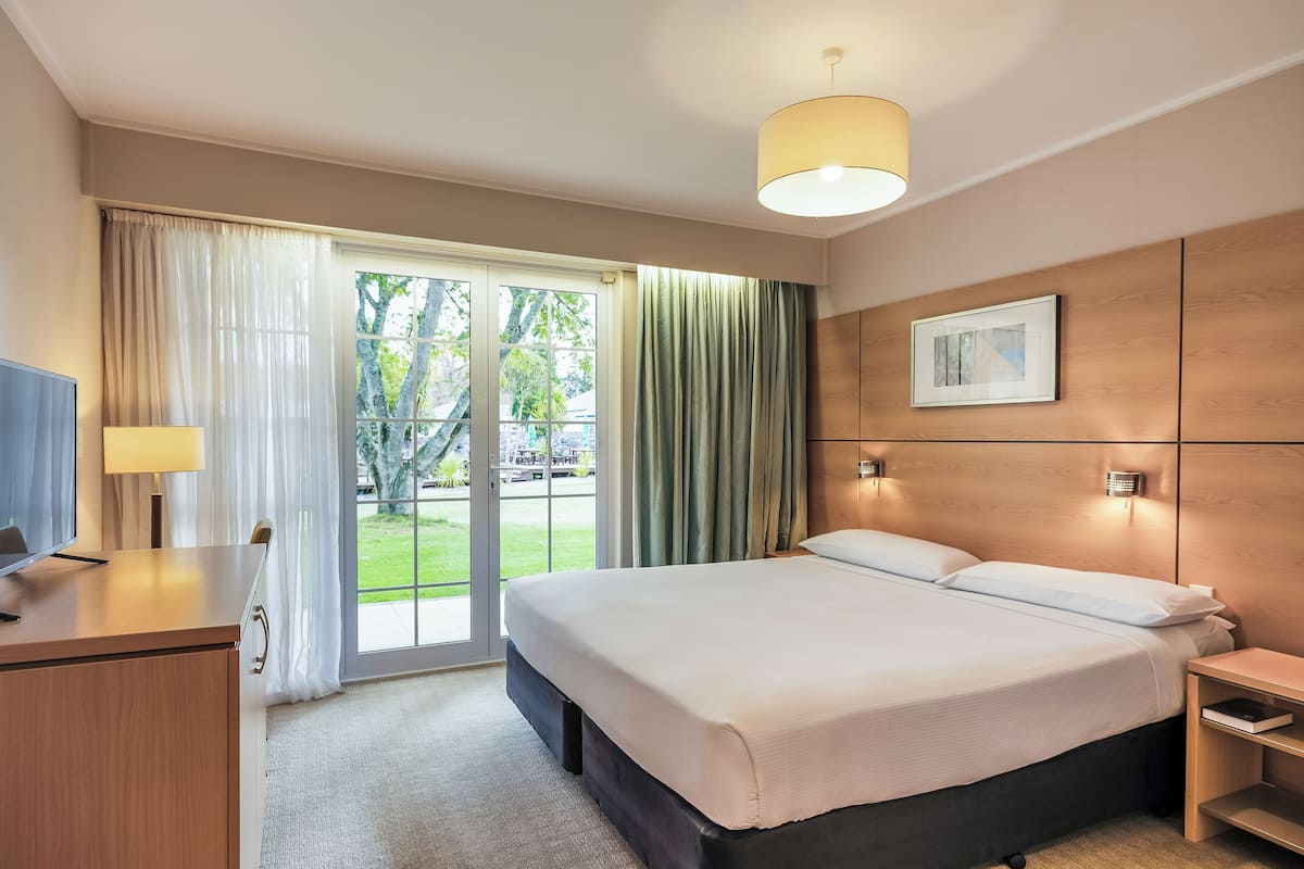Een hotelkamer met een bed, een bureau, een televisie, een raam met gordijnen en een schilderij aan de muur.