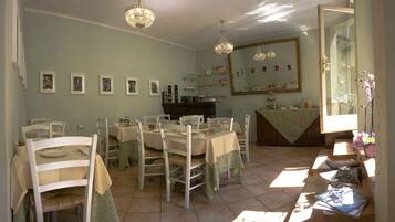 Zona pranzo con diversi tavoli e sedie, un lampadario, uno specchio grande e una finestra con luce solare.