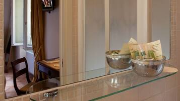 A bathroom with a glass shelf holding toiletries, a mirror, and a bathtub.