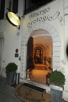La entrada del Albergo Orlogio, con un arco de piedra, un felpudo y plantas en macetas.