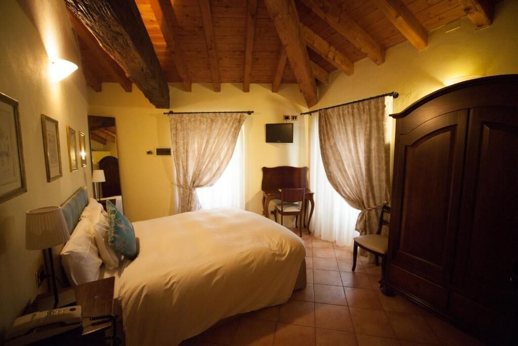 A bedroom with a large bed, wooden wardrobe, and a desk with a lamp.