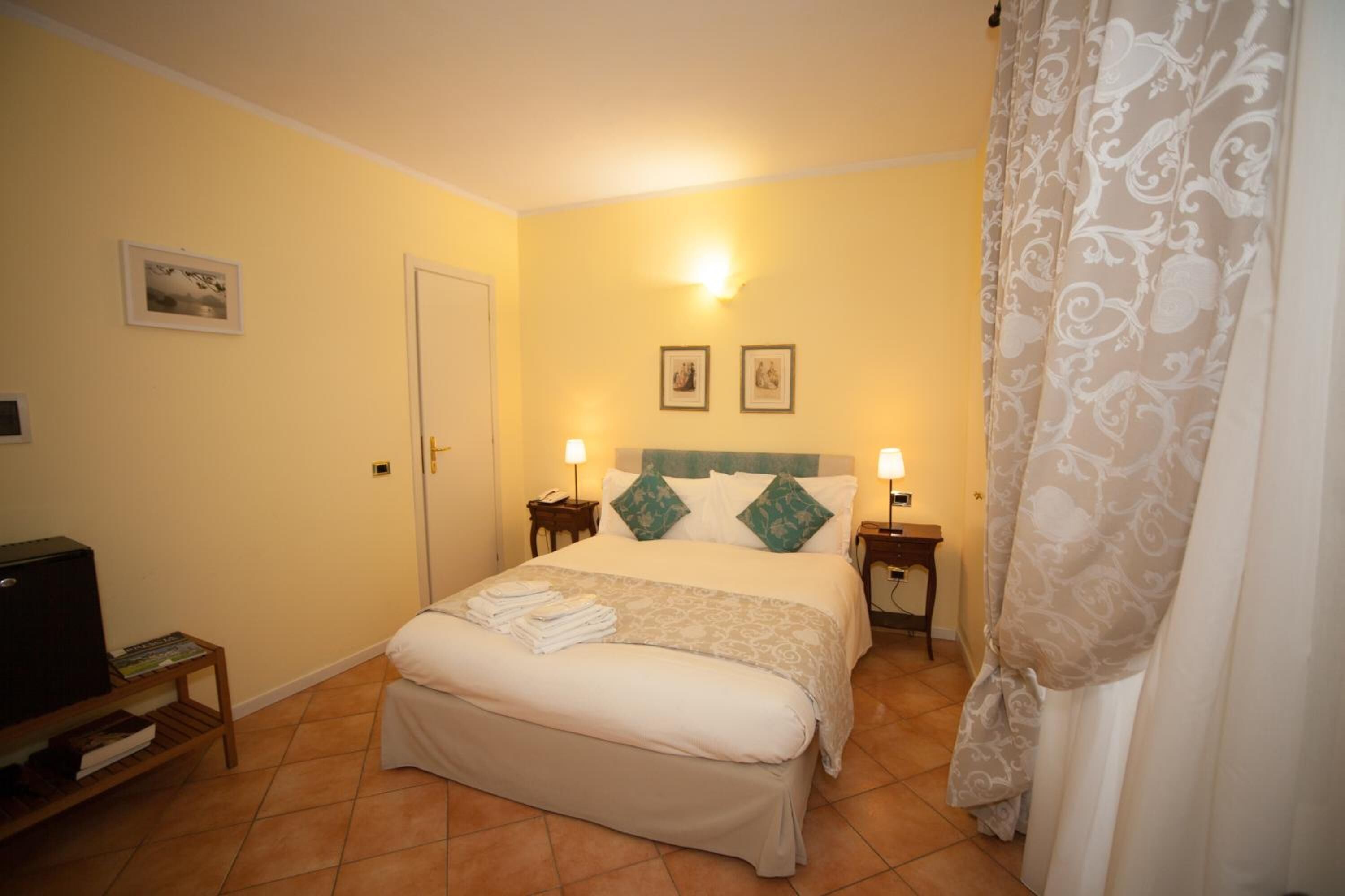 Ein Hotelzimmer mit einem Bett, zwei Nachttischen mit Lampen, einem Fernseher und einer Tür.