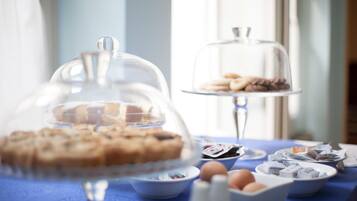 Un bufé de desayuno con diversas pastelerías y productos horneados bajo campanas de vidrio, dispuesto sobre una mesa con mantel azul.