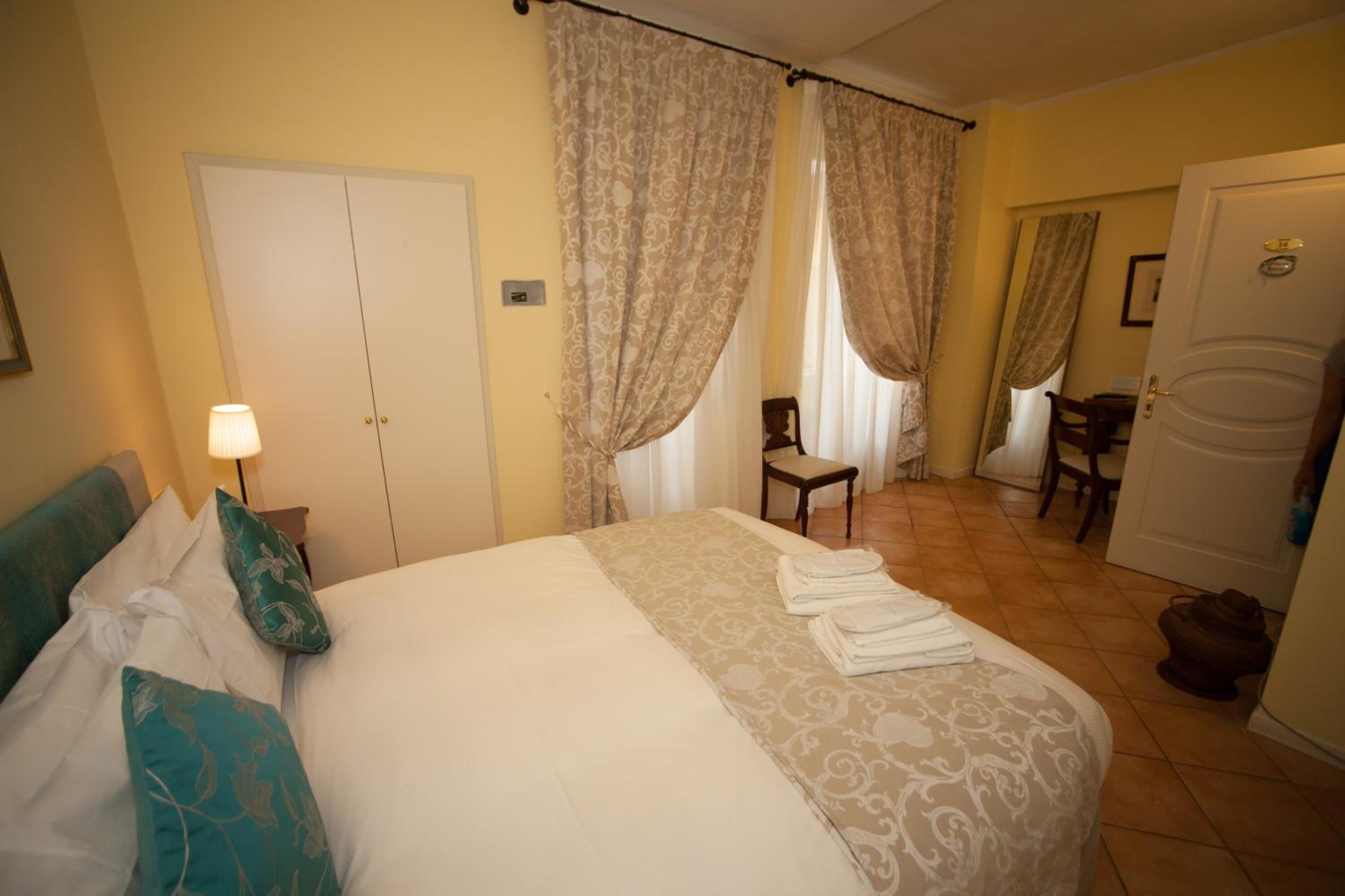A hotel room with a bed, a chair, a desk, and a wardrobe.