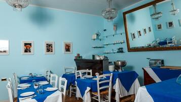 Un espace repas avec des nappes bleues, des chaises blanches et un grand miroir au mur.