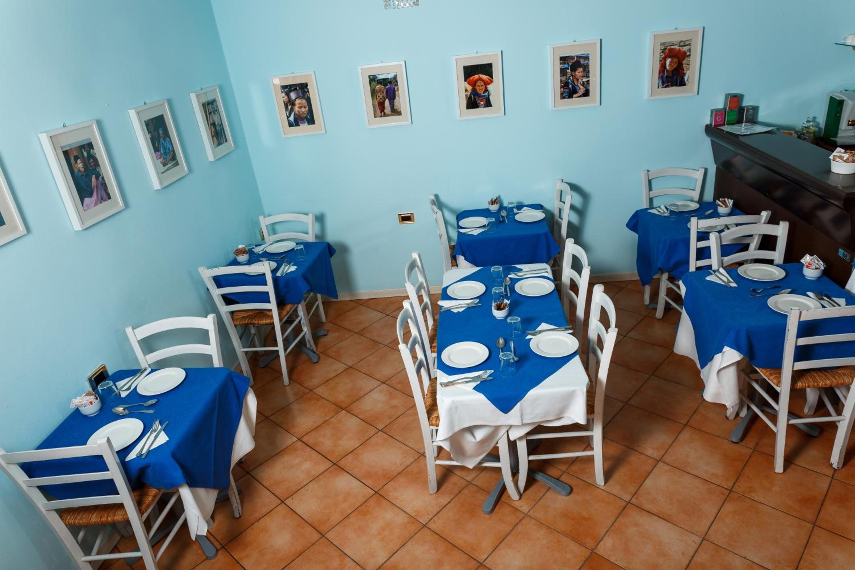 Comedor con varias mesas dispuestas para comidas, cada una con sillas blancas y manteles azules.
