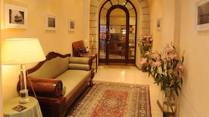 A hotel lobby with a sofa, a table with a lamp, a patterned rug, and a vase with flowers. - Albergo Orologio (Brescia)