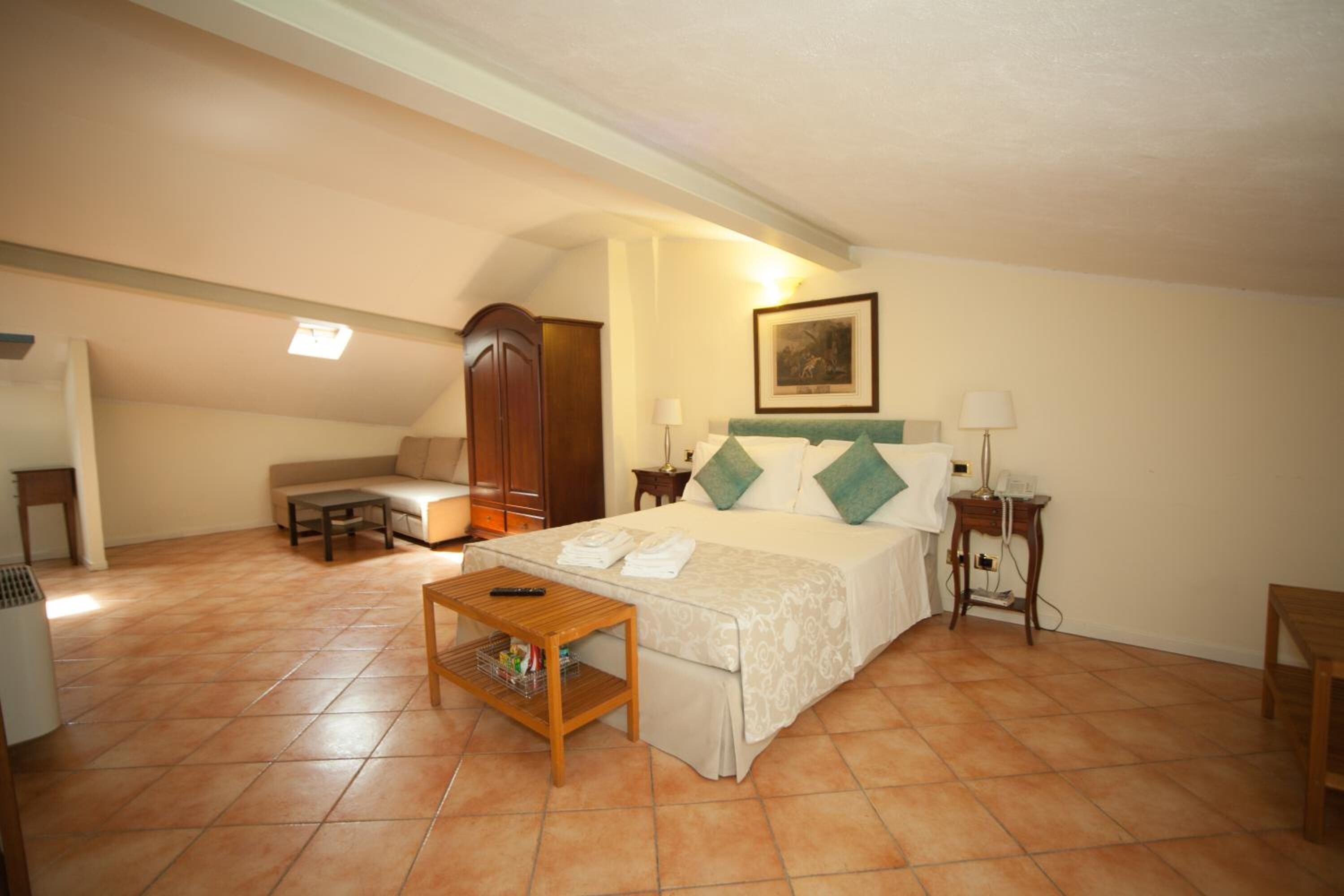 A hotel room with a bed, a sofa, a wooden table, a lamp, and a painting on the wall.