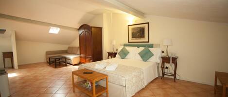 A hotel room with a bed, a sofa, a wooden table, a lamp, and a painting on the wall.