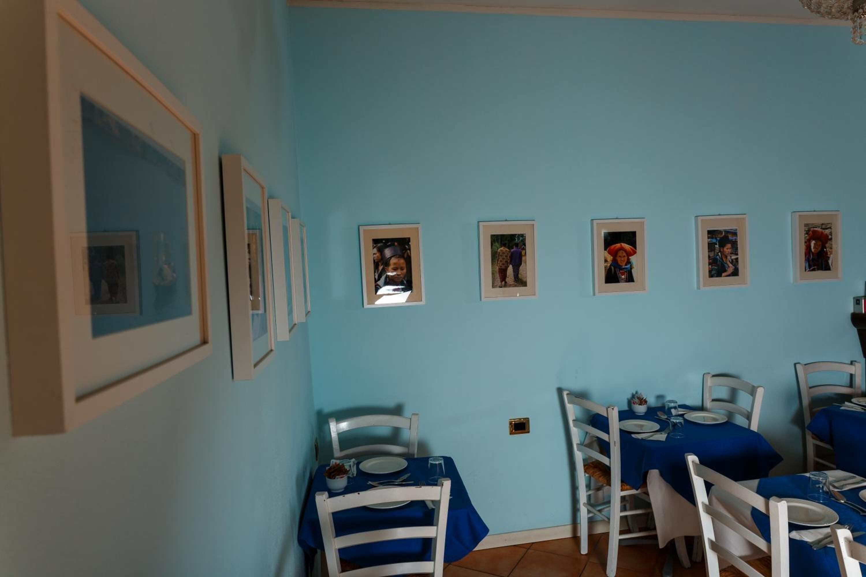 Ein Essbereich mit blauen Tischdecken, weißen Stühlen und gerahmten Bildern an der Wand.