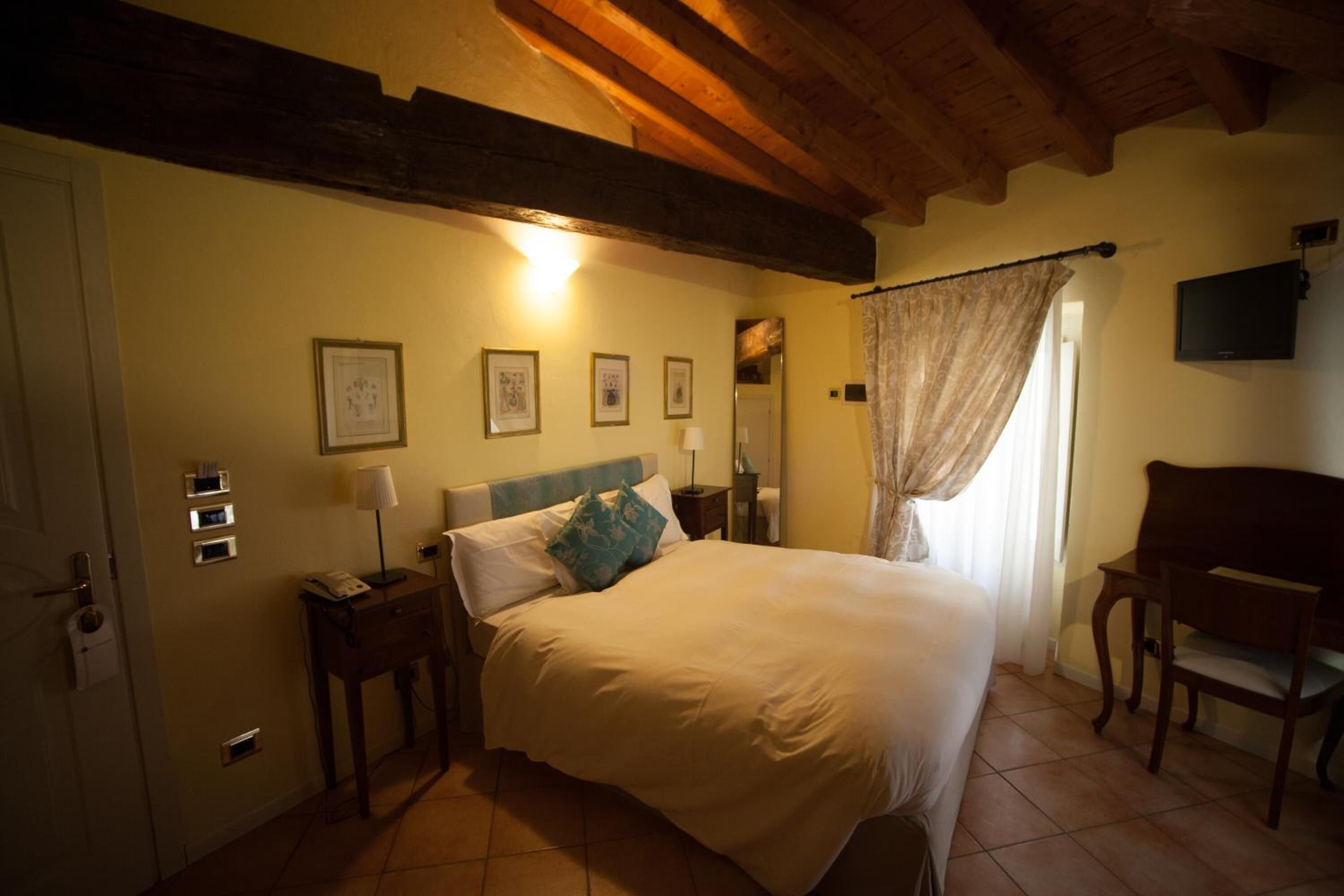 A bedroom with a bed, bedside tables, a desk, a chair, a TV, and a window with curtains.