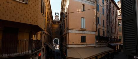 Une rue étroite bordée de bâtiments des deux côtés, un escalier menant à une arche centrale et des espaces aménagés pour s’asseoir à l’extérieur.
