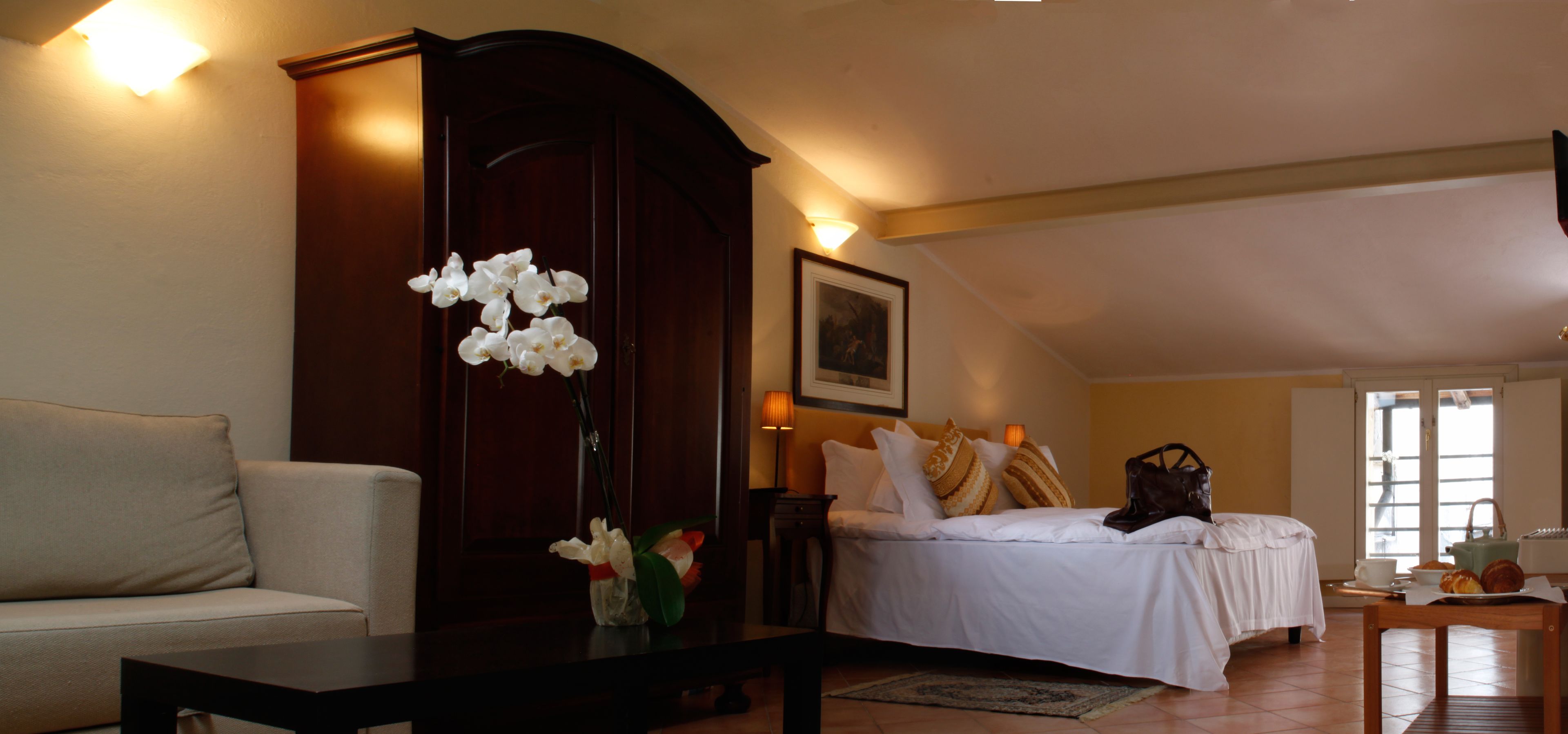 Un dormitorio con cama, mesita de noche, cómoda y un jarrón de flores blancas.