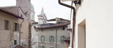 Un balcone con tegole in terracotta, ringhiera in metallo e vista su edifici storici con una torre e una struttura a cupola sullo sfondo.
