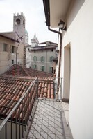 Un balcón con tejas de terracota, barandilla metálica y vista de edificios históricos con una torre y una estructura con cúpula al fondo.
