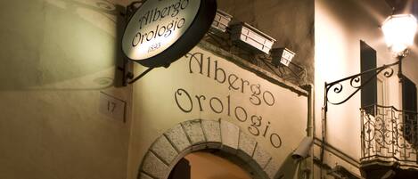 The exterior of Albergo Orologia, featuring an arched entrance, a signboard, and a potted plant.