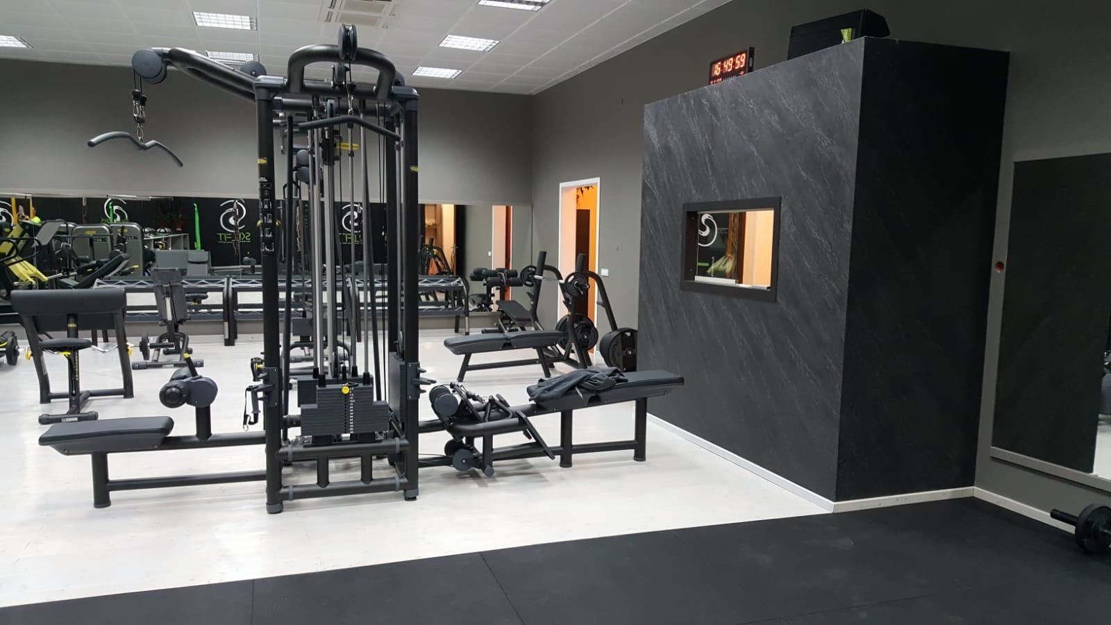 A gym with various exercise machines, benches, and a digital clock displaying 15:49:59.
