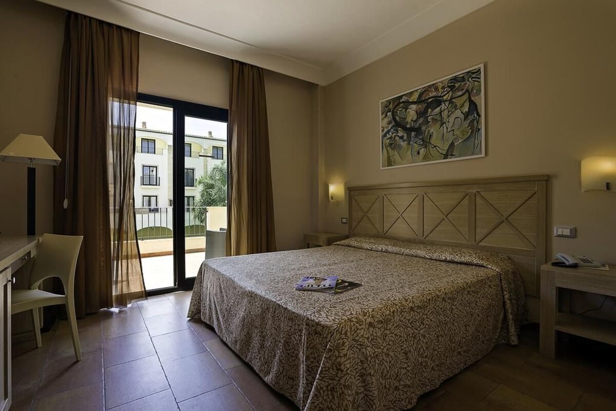 Habitación de hotel con cama, escritorio, silla, un cuadro en la pared y vistas al exterior.