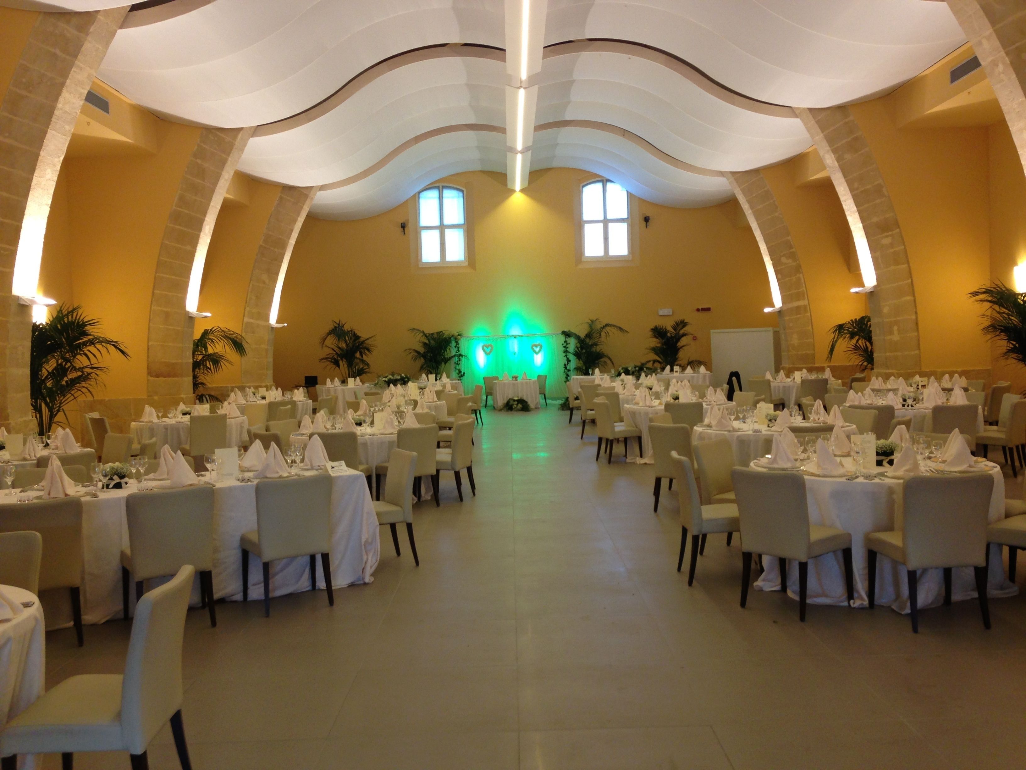 A banquet hall with round tables set for dining, featuring a high arched ceiling and large windows.