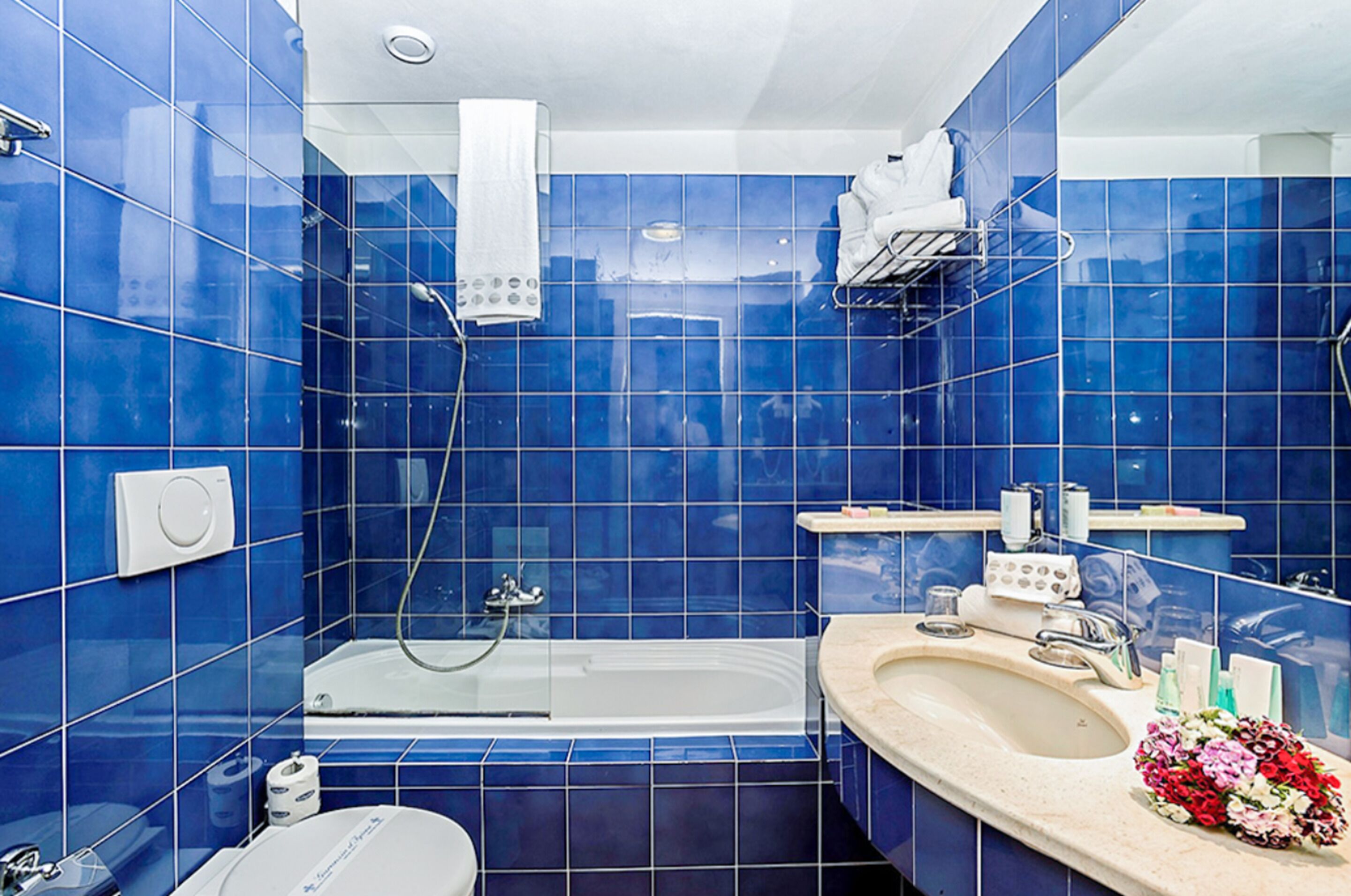 Een badkamer met blauwe tegels, een badkuip, een toilet en een wastafel met een bloemenboeket.