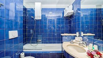 Een badkamer met blauwe tegels, een badkuip, een toilet en een wastafel met een bloemenboeket.