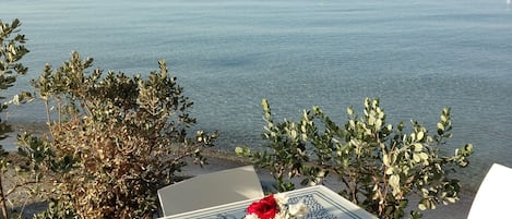 Une table recouverte d’une nappe à motifs bleus et blancs, un vase rempli de fleurs et une vue sur la mer.