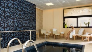 A spa area with a pool, lounge chairs, and a wall with a mosaic pattern. - Mahara Hotel & Wellness (Mazara del Vallo)
