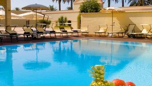 A swimming pool with lounge chairs and umbrellas, surrounded by palm trees. - Mahara Hotel & Wellness (Mazara del Vallo)