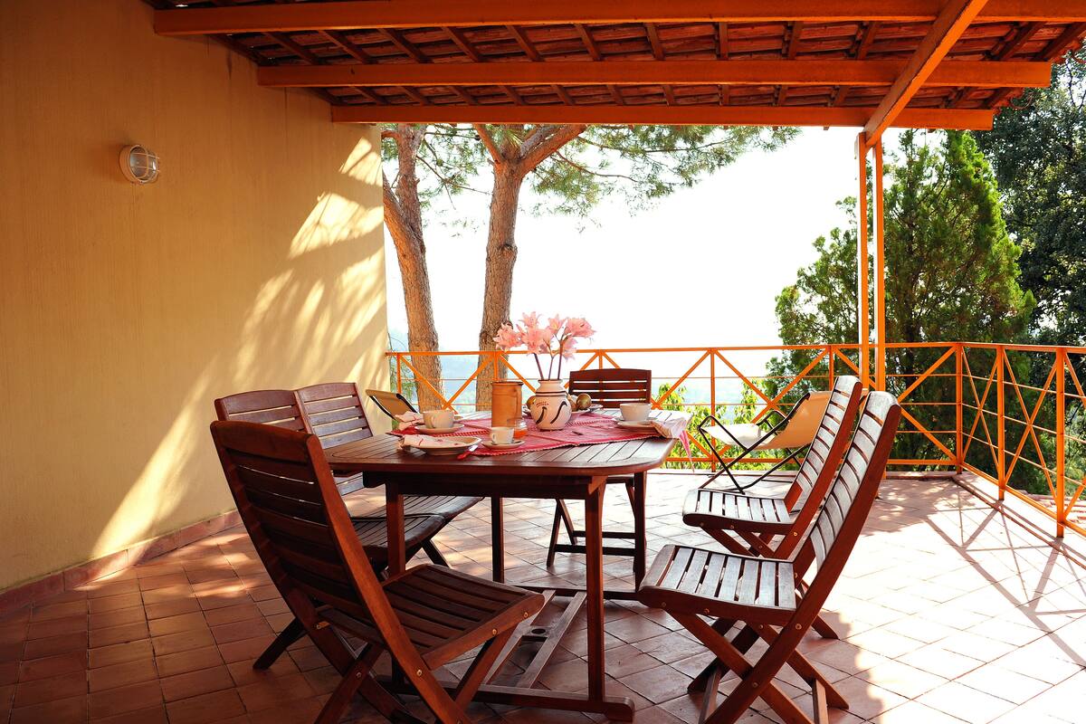 A wooden table and chairs set on a tiled patio with a view of trees and a railing.