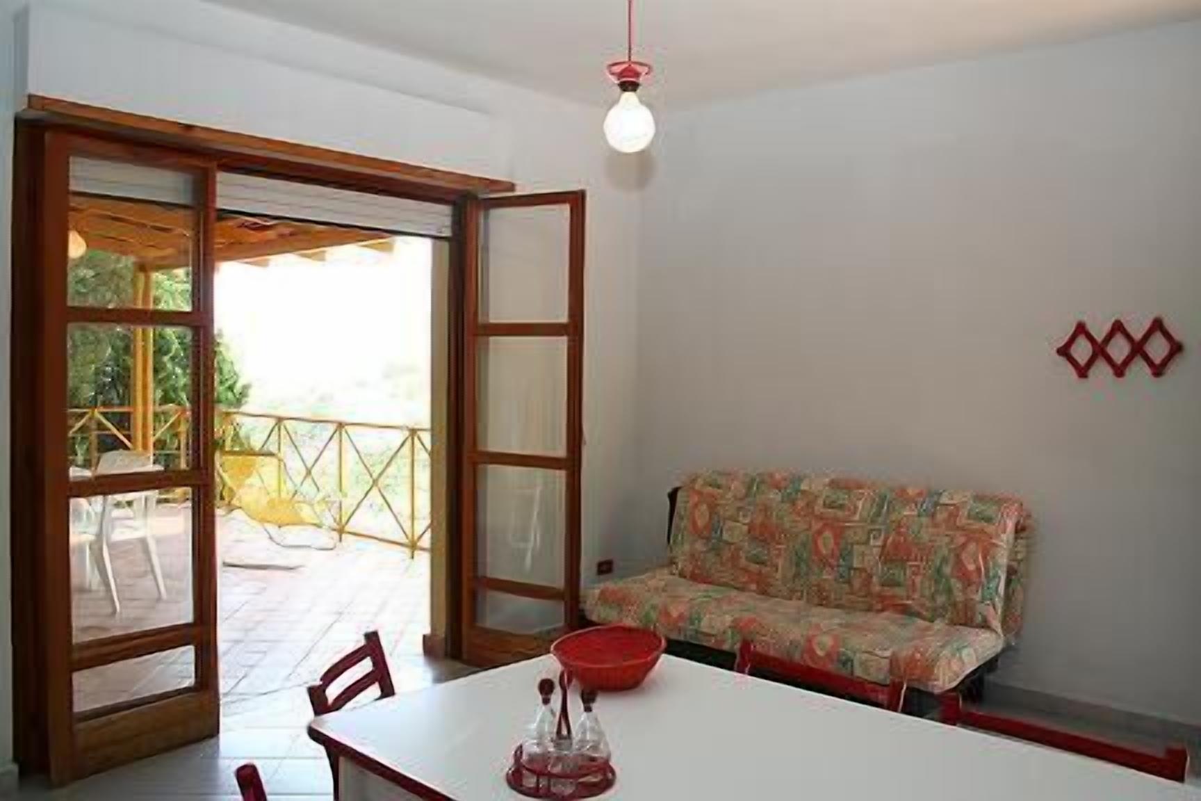 Quarto com uma mesa de jantar, um sofá e uma porta de vidro deslizante que dá para área externa com corrimão amarelo.