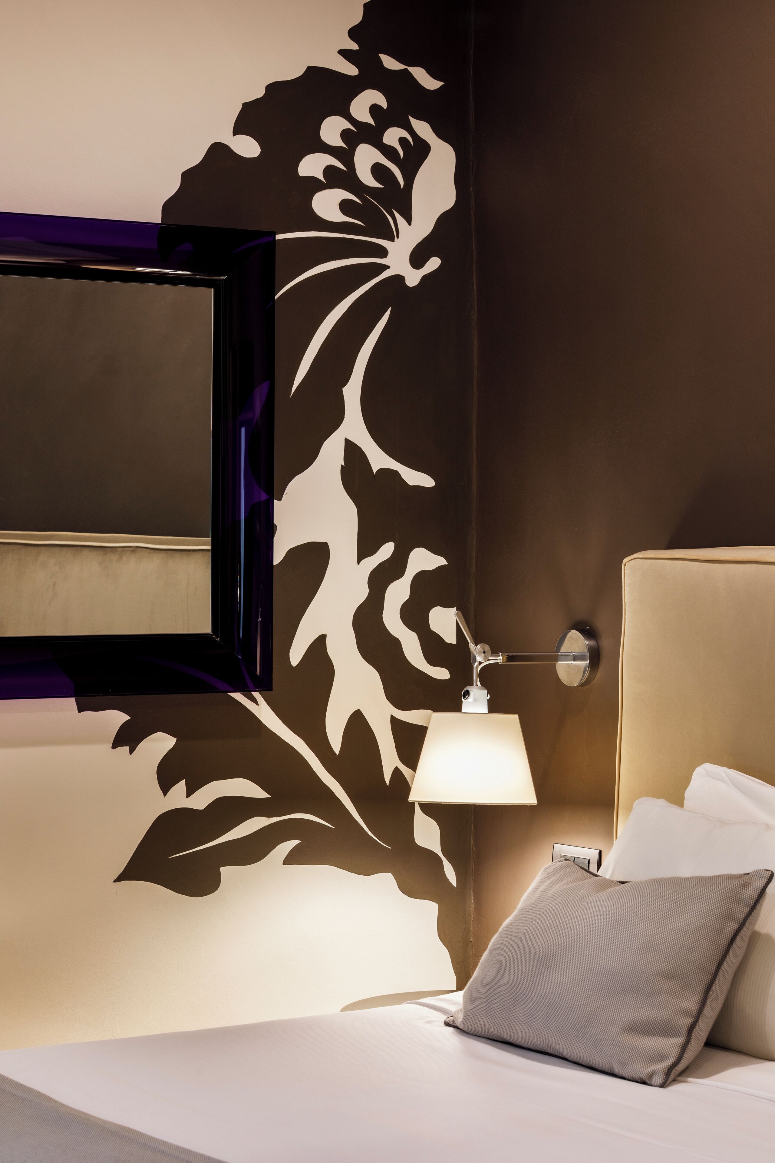 A hotel room with a bed, a nightstand, a lamp, and a wall with a decorative pattern.