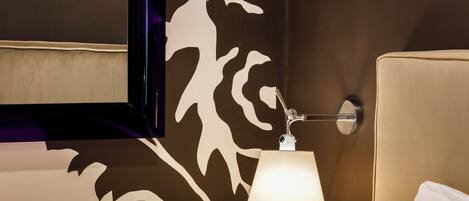 A hotel room with a bed, a nightstand, a lamp, and a wall with a decorative pattern.