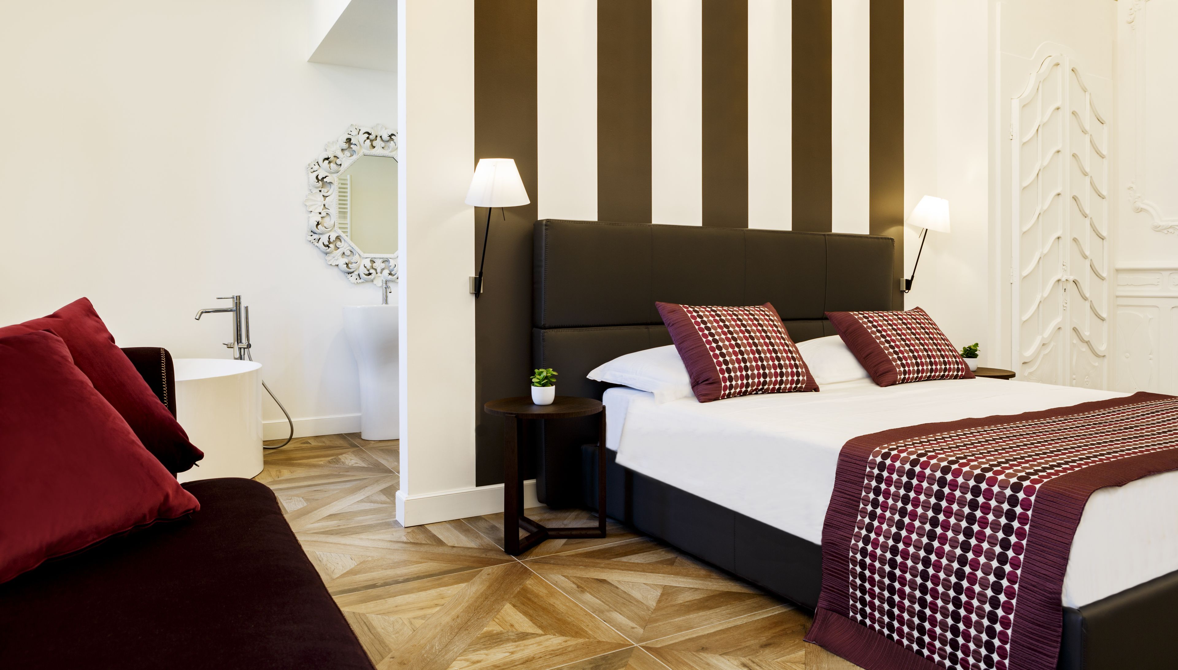 Una camera d'albergo con un letto grande, due abat-jour, un tavolino con una pianta e uno specchio decorativo.
