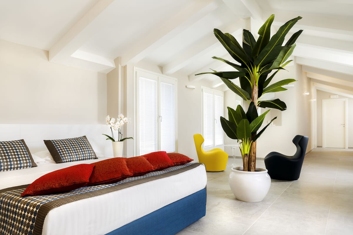 A modern bedroom with a large bed, a potted plant, and a bright yellow chair.