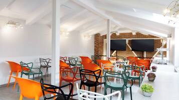 A modern indoor space with a high ceiling, exposed brick walls, and a row of colorful chairs.