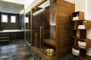 Un baño moderno con ducha envuelta en vidrio, tocador de madera y estante empotrado con toallas.