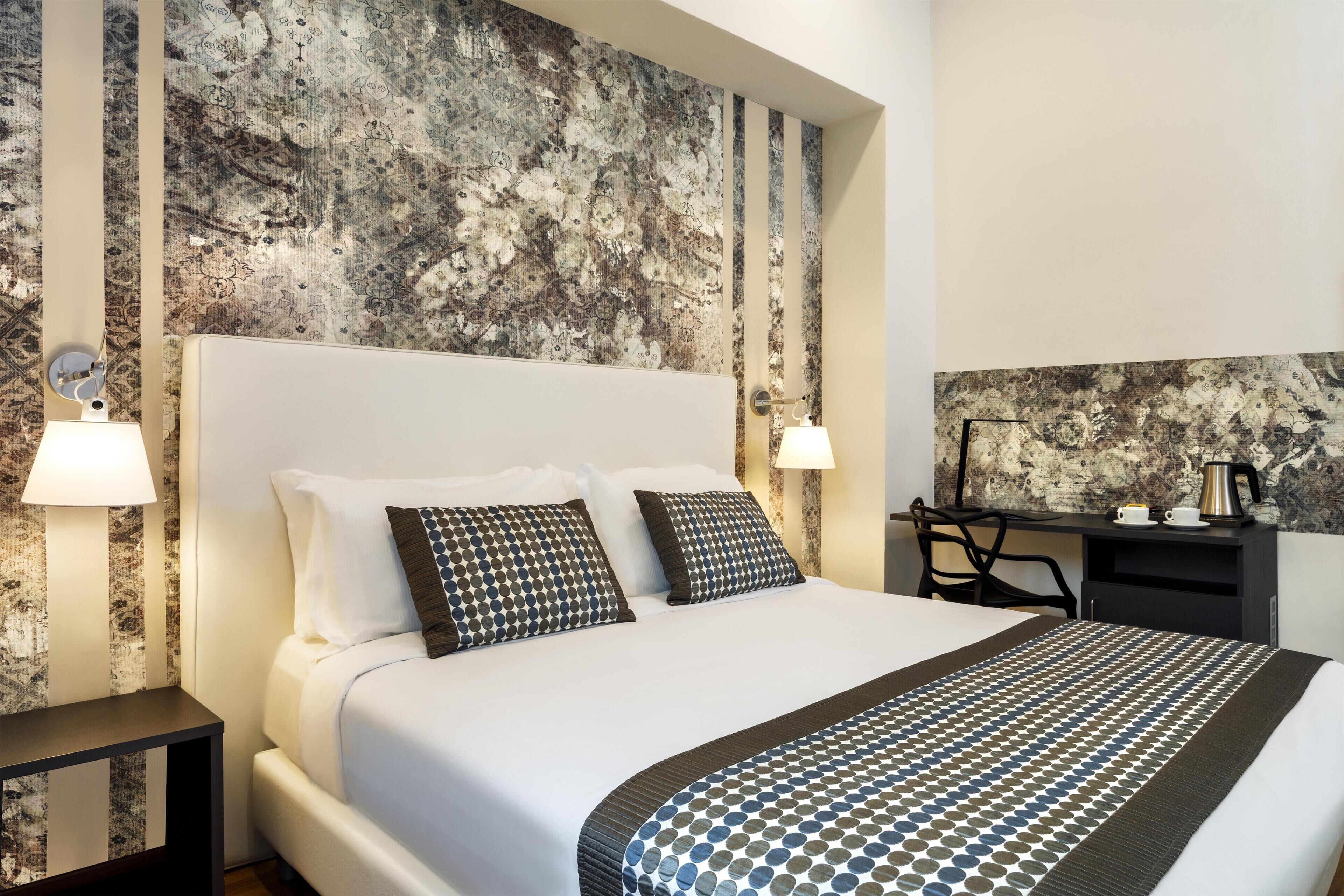 Une chambre d’hôtel avec un grand lit, deux lampes de chevet, un bureau avec une machine à café et un mur décoré d’un motif.