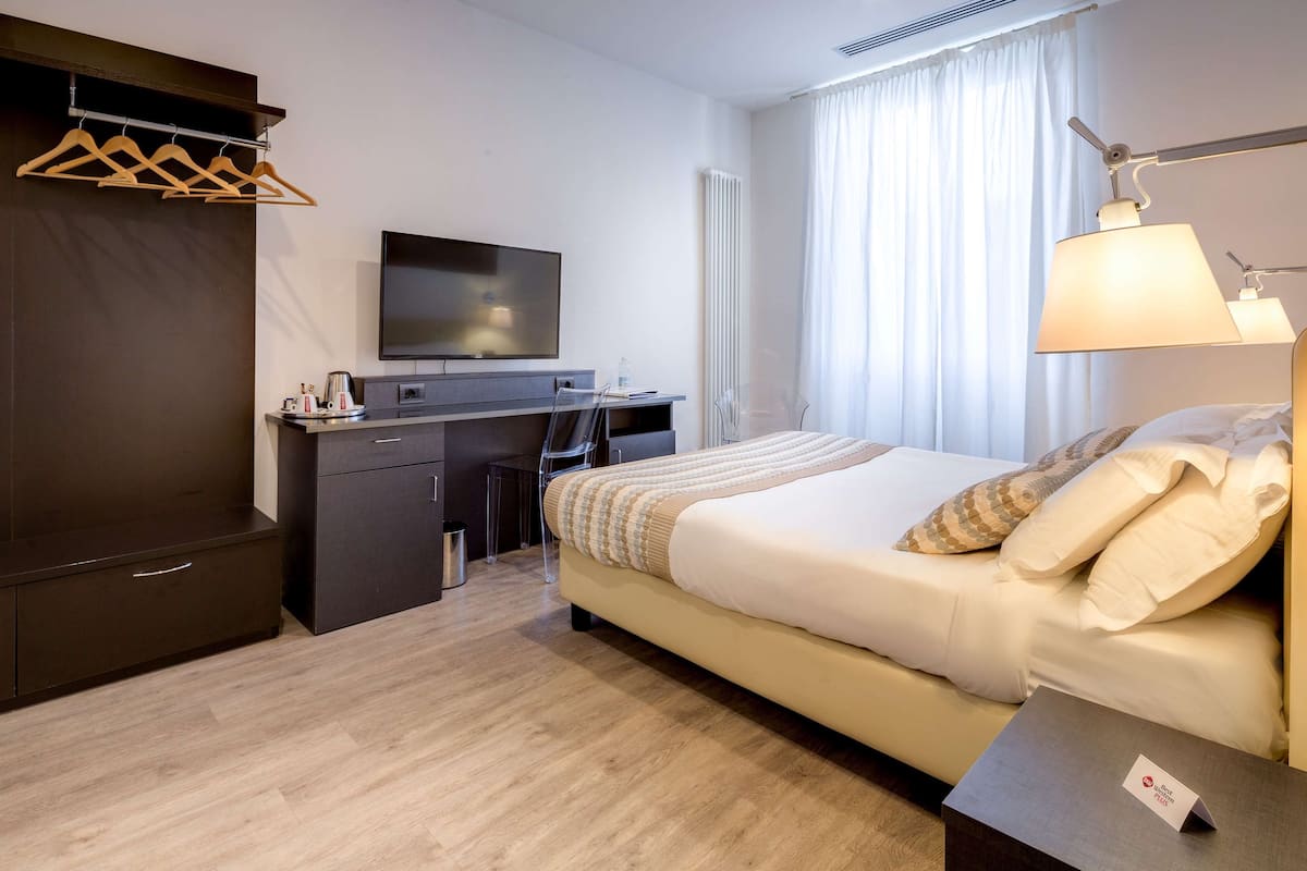 A hotel room with a bed, a desk, a TV, a wardrobe, and a lamp.