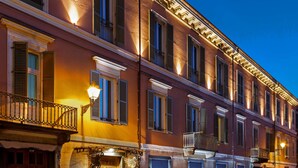 Un immeuble à plusieurs étages, de style architectural classique, caractérisé par des fenêtres régulièrement espacées et un balcon doté d’une balustrade en fer forgé.